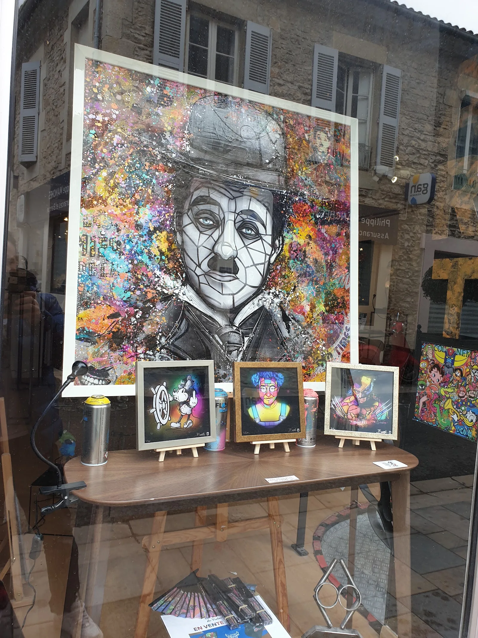 Vitrine de l'atelier : un grand portrait de Charlie Chaplin en mosaïque et des tirages encadrés présentés à la vente